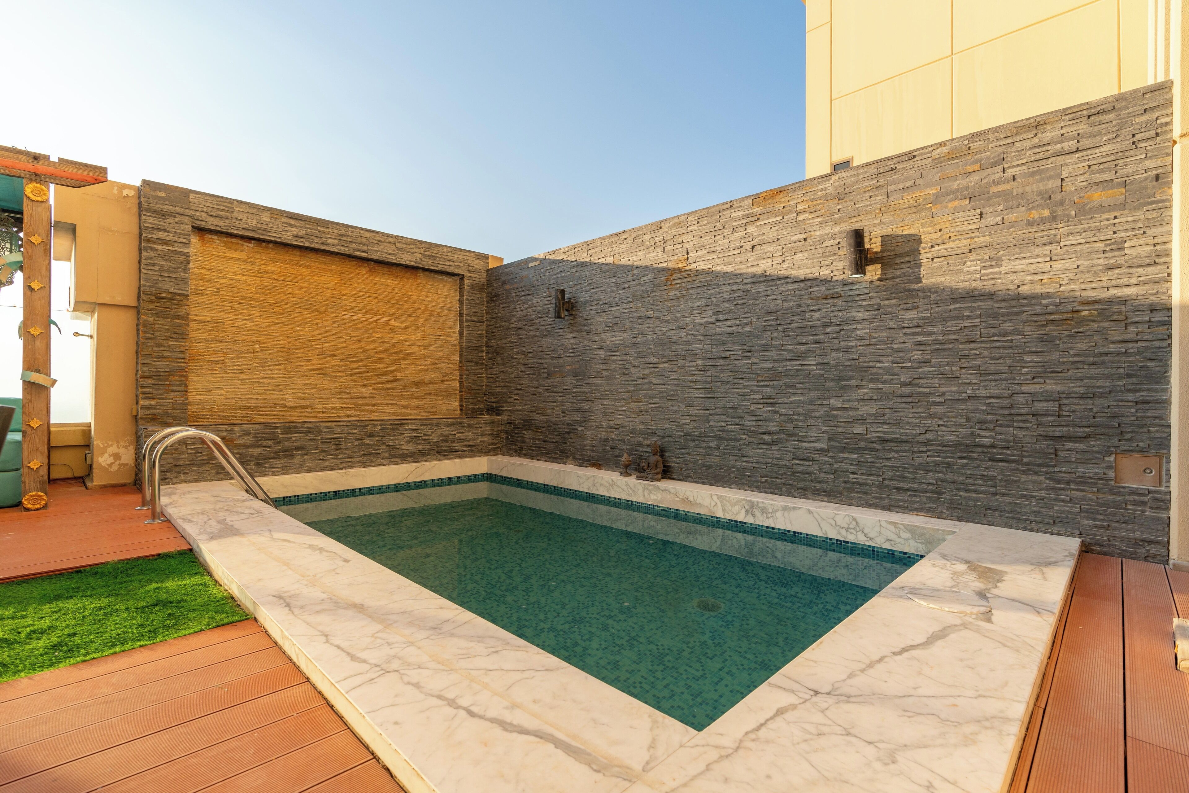 A rectangular swimming pool with a stone wall and a wooden panel on one side.