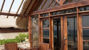 A wooden-framed room with a large glass door, a thatched roof, and a view of the ocean. - Laguava Resort (Rumayla)