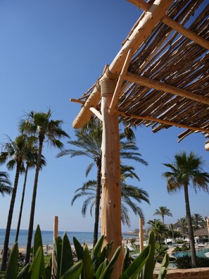 Una estructura de pérgola de madera con vistas a palmeras y una zona de piscina.