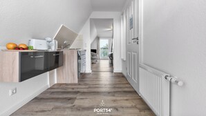 A modern kitchen with a built-in dishwasher, a countertop with fruits, and a view into the dining area. - Apartment 24 - 1-room apartment, TV, shower (Kappeln)