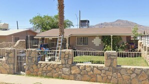 A house with a stone wall, a palm tree, and a mountain in the background. - Bridgeton suites (El Paso)