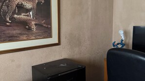 A room with a framed wildlife photograph on the wall, a small black cabinet, and a bed with a floral-patterned bedspread. - Bridgeton suites (El Paso)
