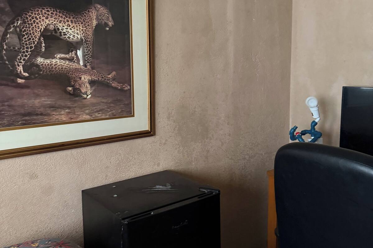 A room with a framed wildlife photograph on the wall, a small black cabinet, and a bed with a floral-patterned bedspread.