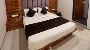 Une chambre moderne avec une tête de lit en bois, un grand lit avec une literie blanche et marron, une table de chevet avec un téléphone et une porte en bois.