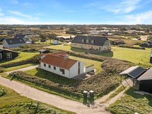 A residential area with houses, a dirt road, and a grassy field.
