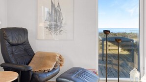Quarto com uma poltrona de couro preto, um banco acolchoado azul e uma obra de arte emoldurada de um veleiro.