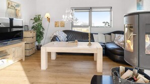 Uma sala de estar moderna com teto de madeira, TV de tela plana, sofá, mesa de centro e lareira a lenha.