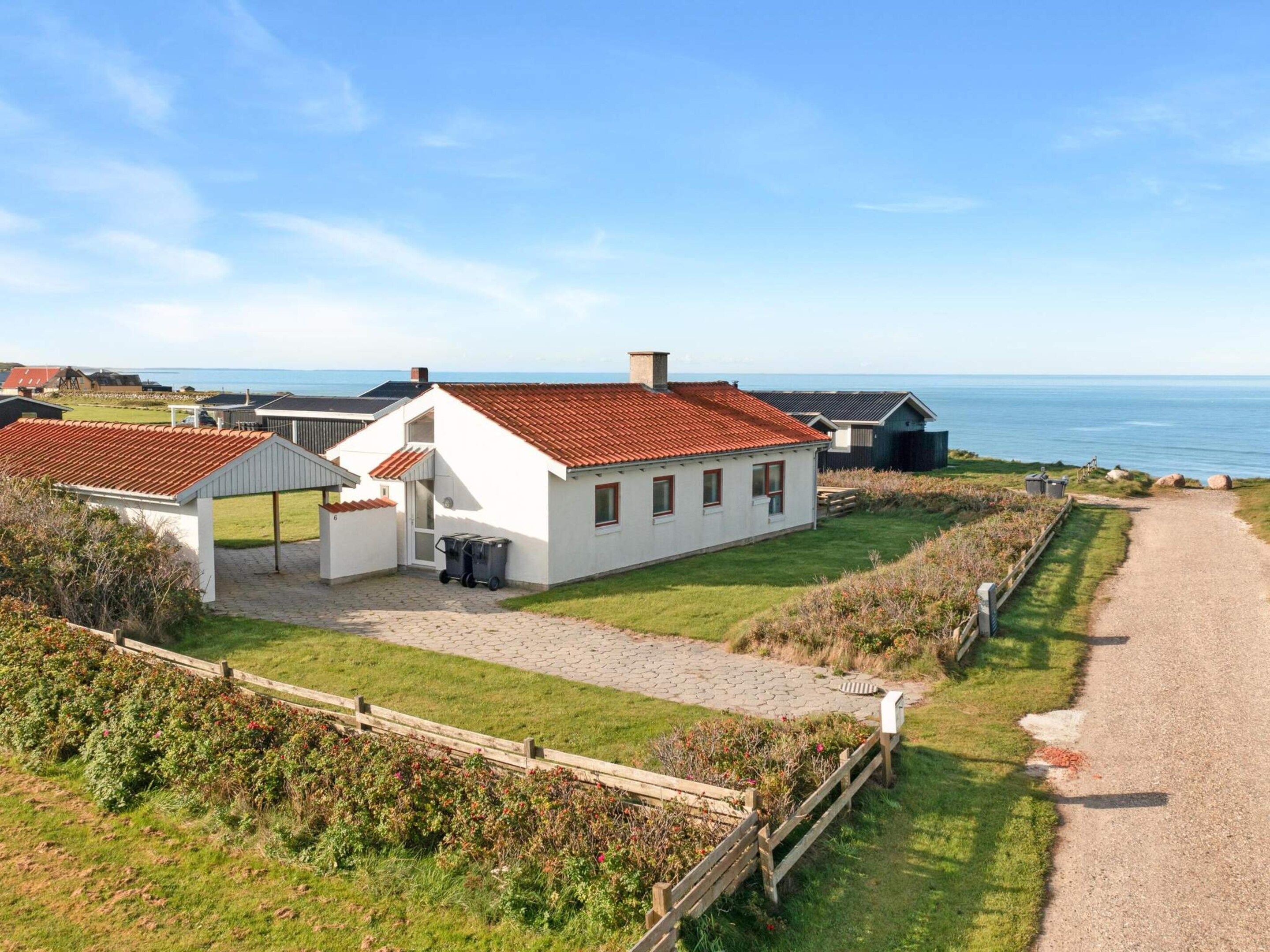 Une propriété située sur la côte, avec un bâtiment blanc, un toit recouvert de tuiles rouges et un chemin de gravier menant à la mer.