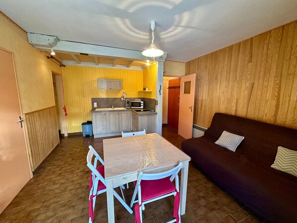 Un espacio habitable compacto con una mesa de comedor, sillas, sofá, kitchenette y una pared revestida de madera.