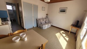 A room with a dining table, chairs, a sofa, a small table with a lamp, and a TV.