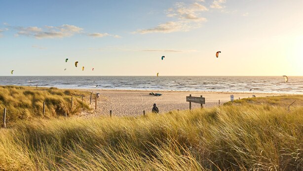 A beach with grassy dunes and a sign indicating 'Plage de la Grande Vilette'.