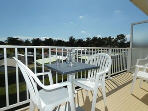 Een balkon met een tafel en twee stoelen, een glas water en uitzicht op de omgeving.