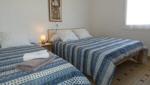 Een kamer met twee bedden, elk voorzien van beddengoed met een patroon, een nachtkastje met een lamp en een lijst met een afbeelding aan de muur.