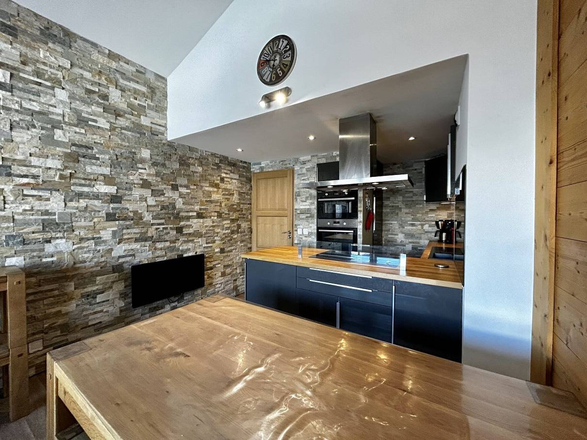 A modern kitchen with a stone wall backsplash, a wooden dining table, and built-in appliances.