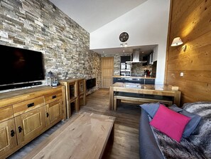 A modern living room with a stone wall, wooden furniture, a flat-screen TV, and a cozy seating area with a fur throw. - Spacious 11 ppl apt, 3 bdr, parking, ski-in/ski-out (Belle Plagne)