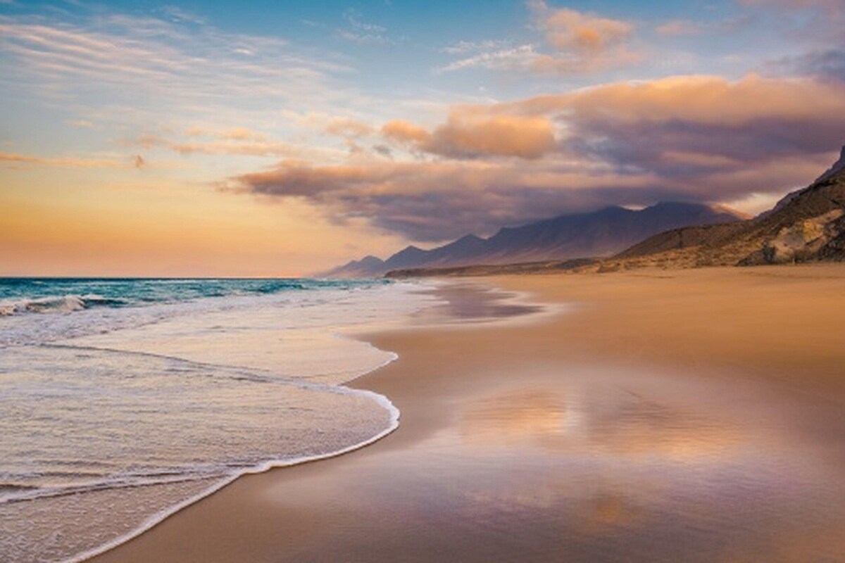 Une plage avec une mer calme, un rivage sablonneux et des montagnes à l’horizon.