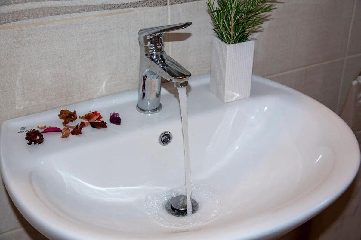 A white sink with running water, a potted plant, and dried flowers on the counter.