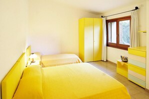 A room with two beds, a window with curtains, a dresser, and a nightstand with a lamp.