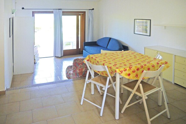 A dining area with a table and chairs, a sofa, a small cabinet, and a sliding glass door leading to an outdoor area. - Apartment in Porto Pollo Near Sea Beach (Palau)