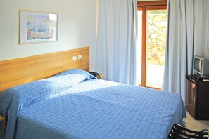 Een slaapkamer met een bed, een schilderij aan de muur, een televisie op een standaard en een stenen muur voor de deur.