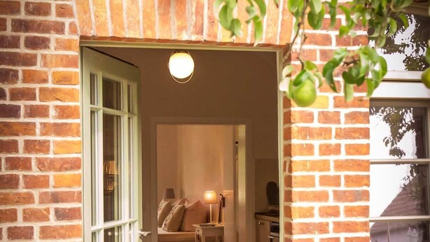 Et murstenshus med en grøn dør, et lille bord med en lampe, og et vindue.