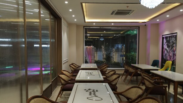A hotel dining area with tables and chairs, a chandelier, and a view through large windows. - Hotel Chandraa Celebration (Dehradun)