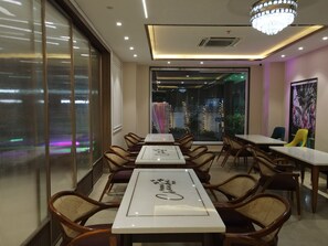 A hotel dining area with tables and chairs, a chandelier, and a view through large windows. - Hotel Chandraa Celebration (Dehradun)