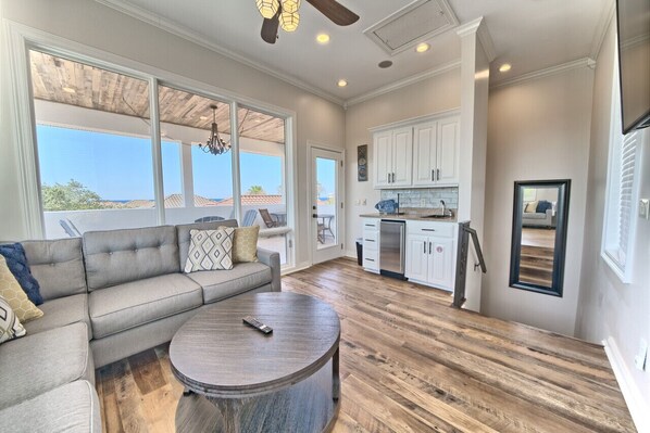 A spacious living area with a large window, a sofa, a coffee table, and a kitchen with white cabinets.