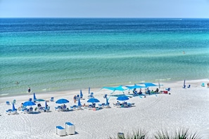 Uma praia com areia branca, águas turquesa cristalinas e guarda-sóis azuis.