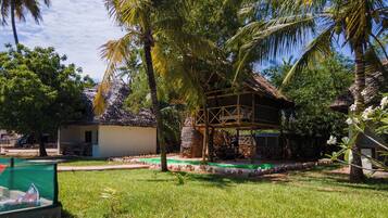 Un resort tropical con una cabaña de techo de paja, una piscina pequeña y abundante vegetación.