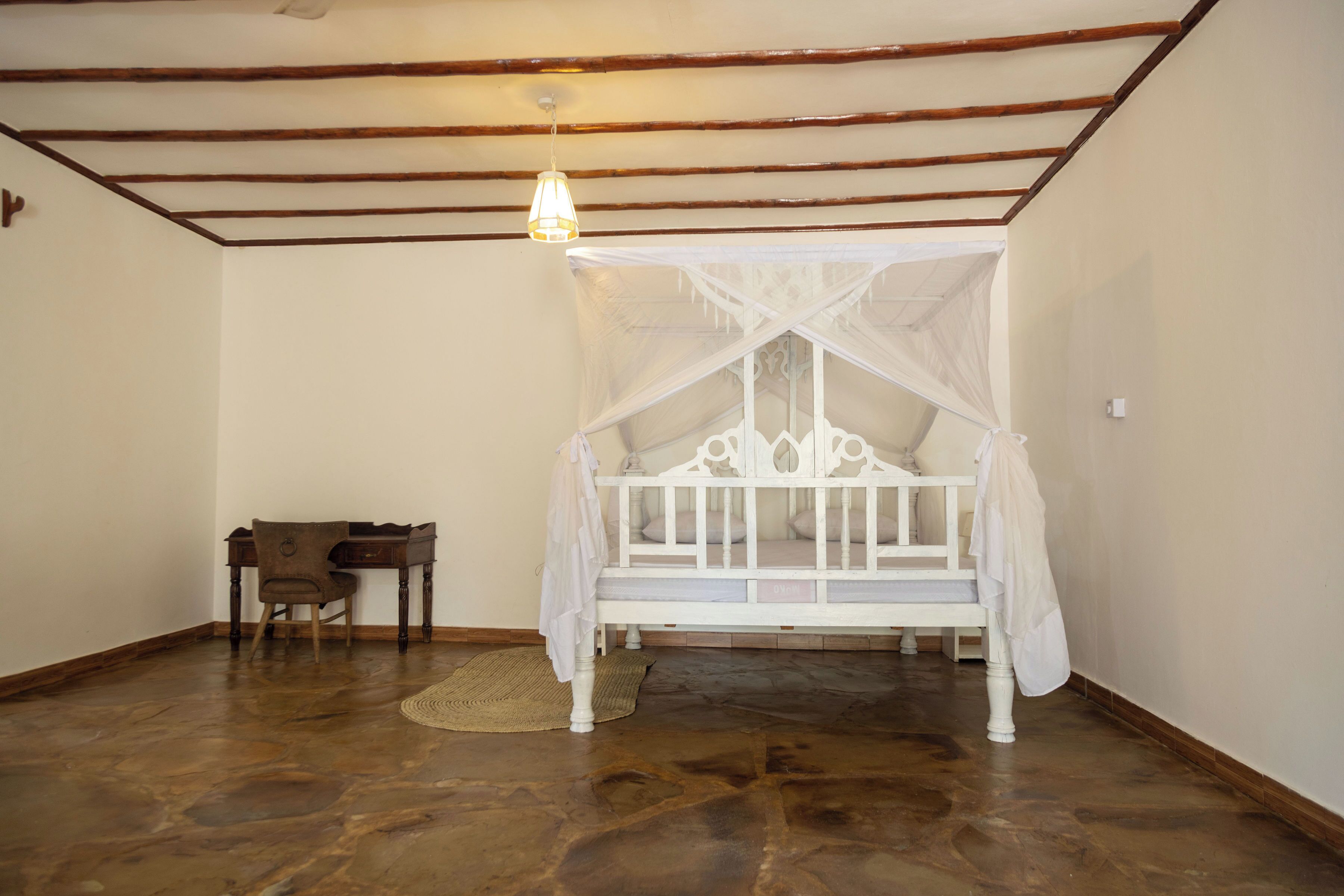 Quarto com cama de dossel branca, escrivaninha de madeira e tapete tecido.