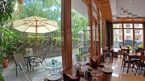 A restaurant with a patio area, tables, chairs, and a large umbrella. - The Seva Hotel (Thimphu)
