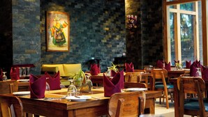 A restaurant with wooden tables and chairs, stone walls, and a large window. - The Seva Hotel (Thimphu)