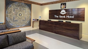 A reception area with a large, intricate wall tapestry, a wooden reception desk, and a sign for The Seva Hotel. - The Seva Hotel (Thimphu)