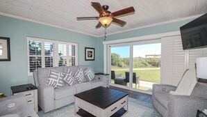 A living room with a grey sofa, a coffee table, and a ceiling fan. There is a sliding glass door leading to an outdoor area.