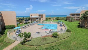 A resort with a central pool, lounge areas, and a view of the ocean.