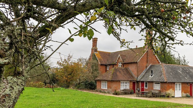 A traditional brick house with a red door, a chimney, and a small garden area with a bench and table. - Tranquil Forest Retreat in Brockenhurst (Brockenhurst)