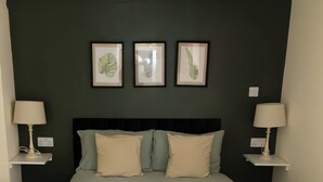 A neatly made bed with a quilted cover, two bedside tables with lamps, and three framed botanical prints on the wall. - Tranquil Forest Retreat in Brockenhurst (Brockenhurst)