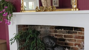A room with a brick fireplace, a Buddha statue, and various potted plants. - Tranquil Forest Retreat in Brockenhurst (Brockenhurst)