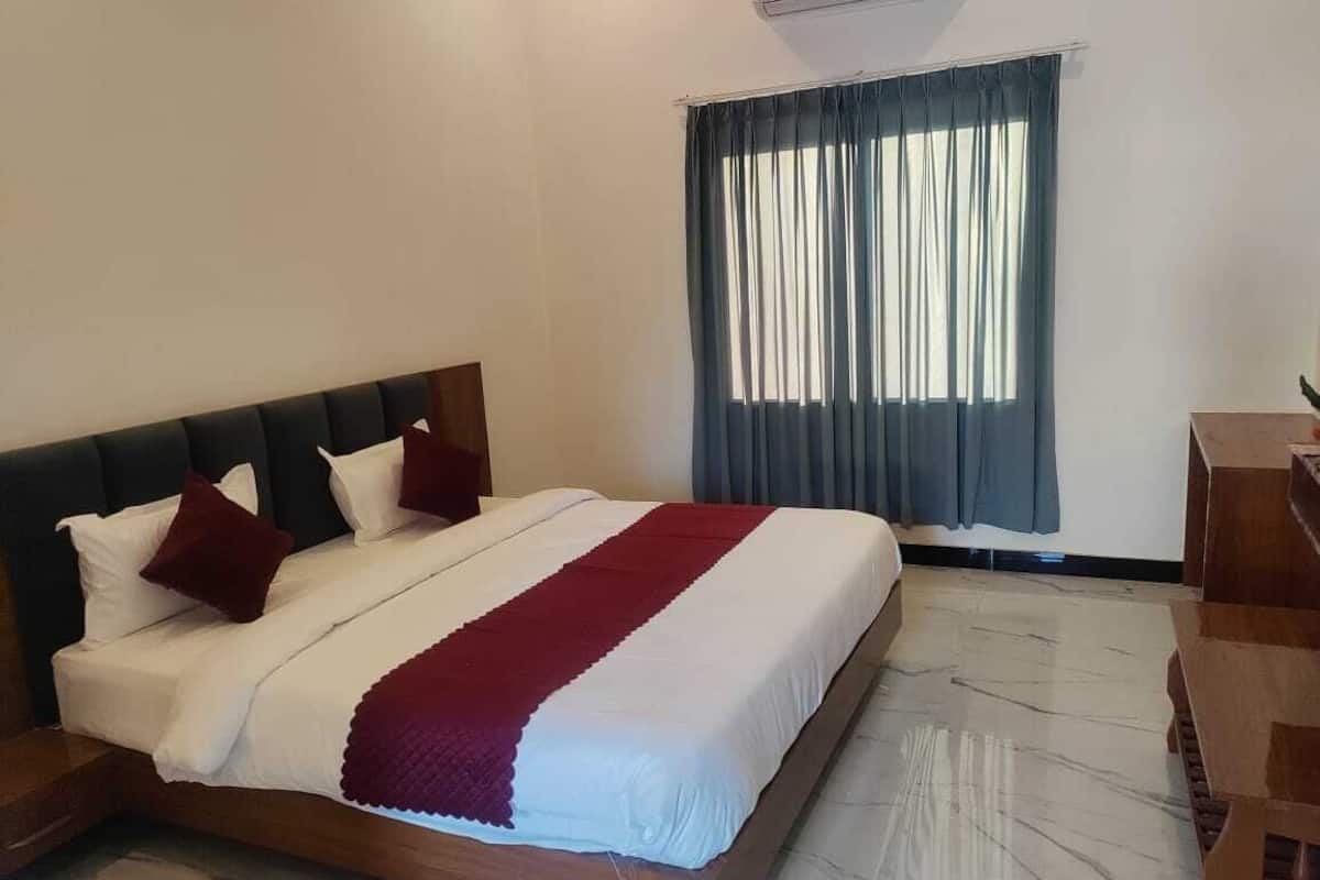 A neatly made bed with white and red bedding, a wooden headboard, and a wooden nightstand with a lamp.