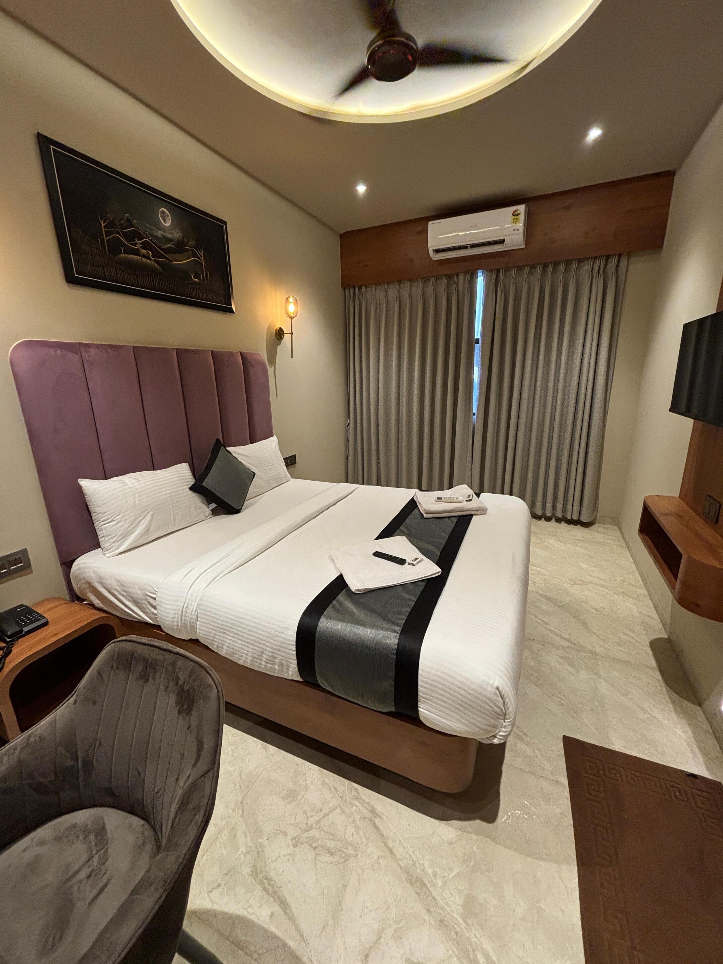 Una habitación de hotel moderna con una cama grande, cabecera, mesita de noche con teléfono, una silla y un ventilador de techo.