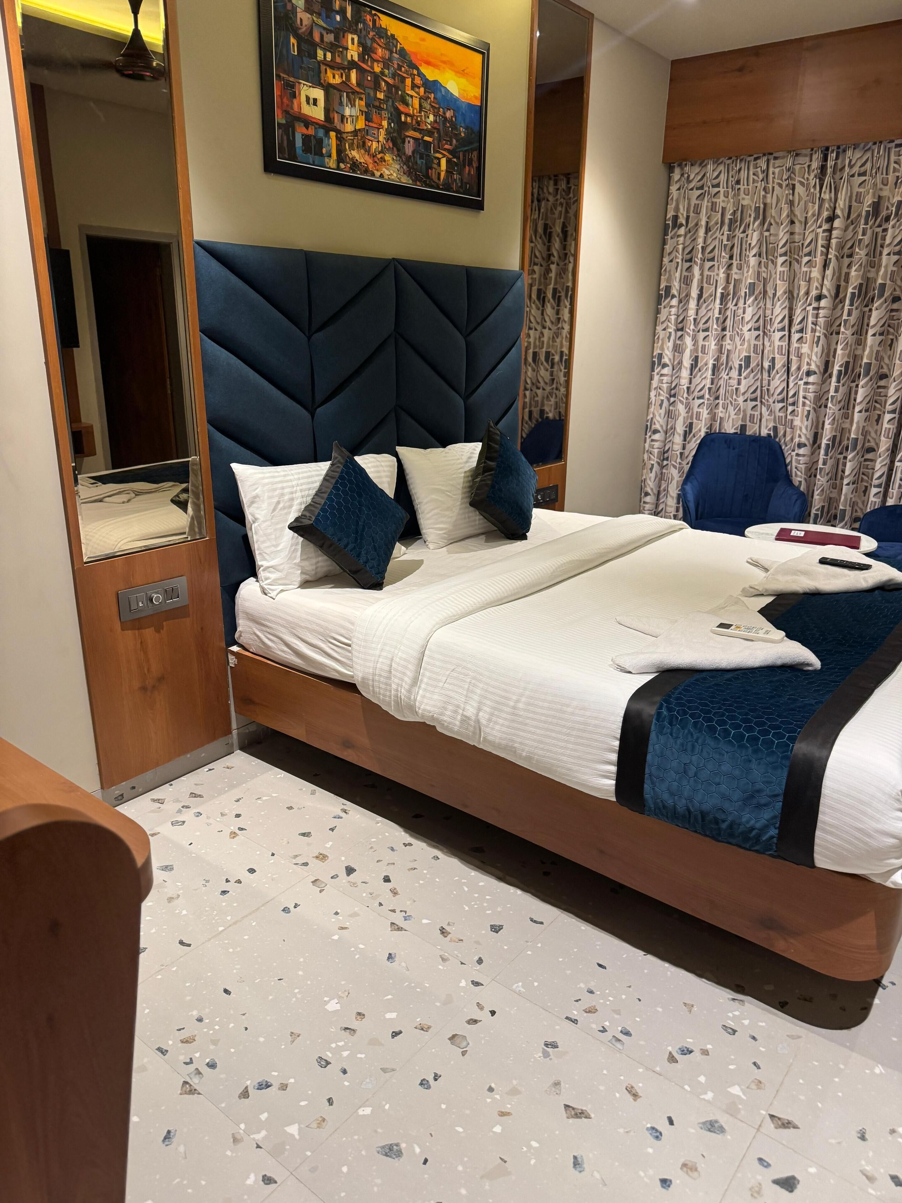 Habitación de hotel moderna con una cama grande, cabecera con diseño geométrico, un cuadro sobre la cama y una cortina estampada.