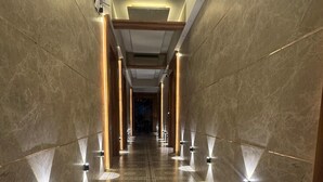 A long, narrow hallway with patterned carpet, illuminated by wall-mounted lights, and flanked by marble walls. - Hotel Regalia Suites (Navi Mumbai)