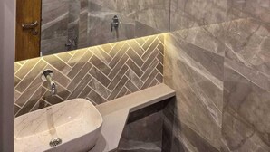 A modern bathroom with a marble wall, a sink, and a shower area. - Hotel Regalia Suites (Navi Mumbai)