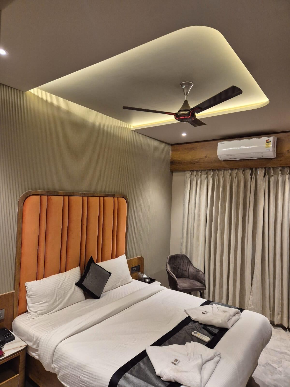 Una habitación de hotel con una cama grande, un ventilador de techo, un equipo de aire acondicionado y una silla.