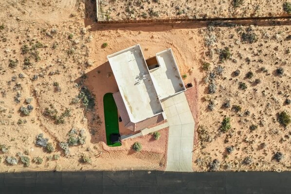 An aerial view of a building with a flat roof, surrounded by sparse vegetation and a dirt ground.