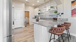 A modern kitchen with a central island, bar stools, and a telescope on the counter. - The Overlook - Hot tub, game room & lake views (Page)