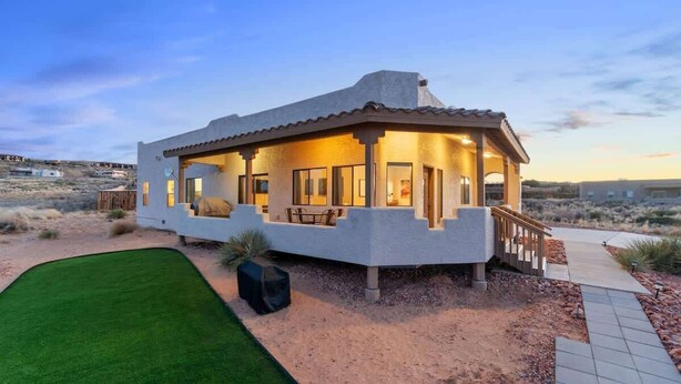 A modern house with a covered patio, a well-maintained lawn, and a desert landscape in the background. - The Overlook - Hot tub, game room & lake views (Page)