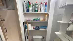 A compact bathroom with a toilet, sink, and shelves containing toiletries. - Cosy Studio Rouen Hôtel de Ville (Rouen)