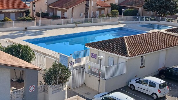 Zona residencial con piscina, vallas blancas y una hilera de edificios de apartamentos al fondo.